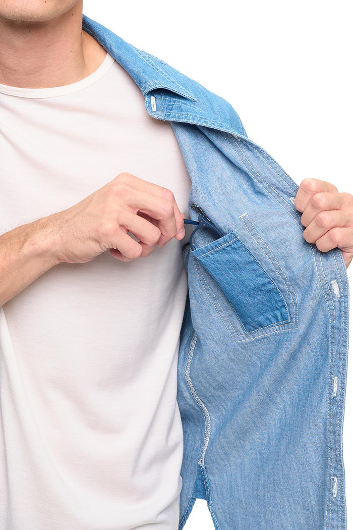 Person in a blue chambray shirt partially open showing an interior pocket with eye glasses.