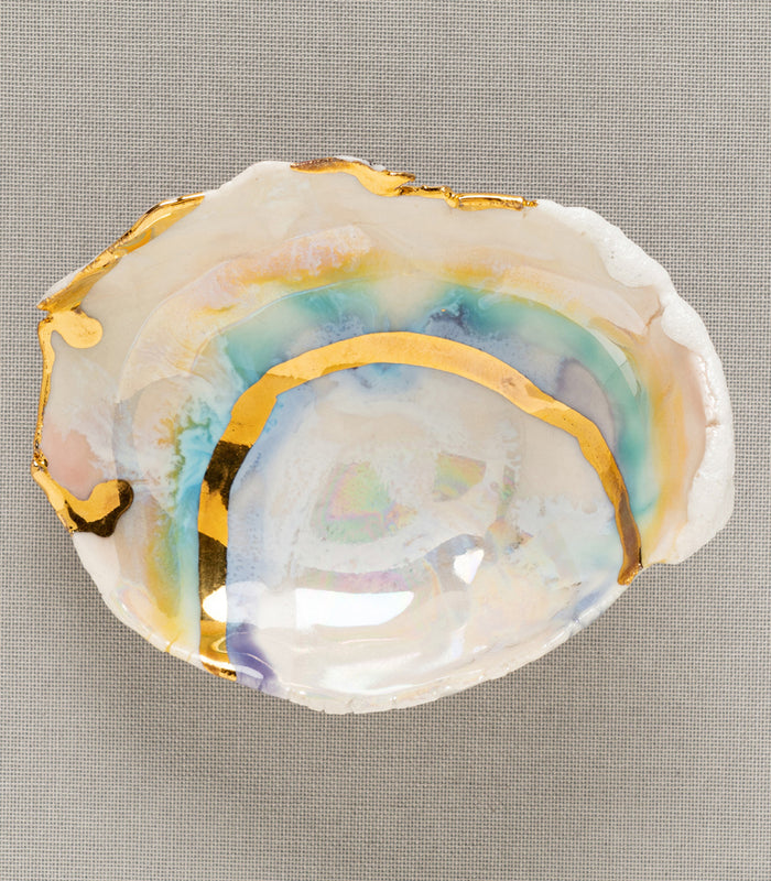 Mini Prism Ring Dish by G-004 shows an iridescent white dish with gold leaf edges on textured fabric.