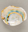 Mini Prism Ring Dish by G-004 shows an iridescent white dish with gold leaf edges on textured fabric.